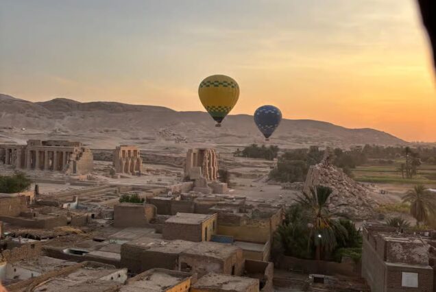 Hot air balloons floating over Luxor, Egypt at sunrise, with views of the Nile River, ancient temples, and desert landscape.