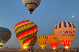 Hot air balloon flying over Luxor, Egypt at sunrise, with the Nile River and West Bank temples visible below.