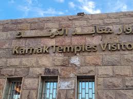 Sign for the Karnak Temples Visitor Center in Luxor, Egypt, displayed on a stone building with English and Arabic text.